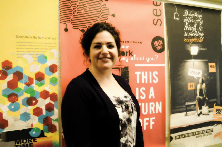 Professor Wendy Shapiro stands in front of posters of her own work, setting an example for students seeking careers in the graphic design field. | Dustin Michelson, staff photographer