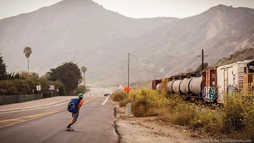 Jin Salamck skateboards the coast of California past a train.