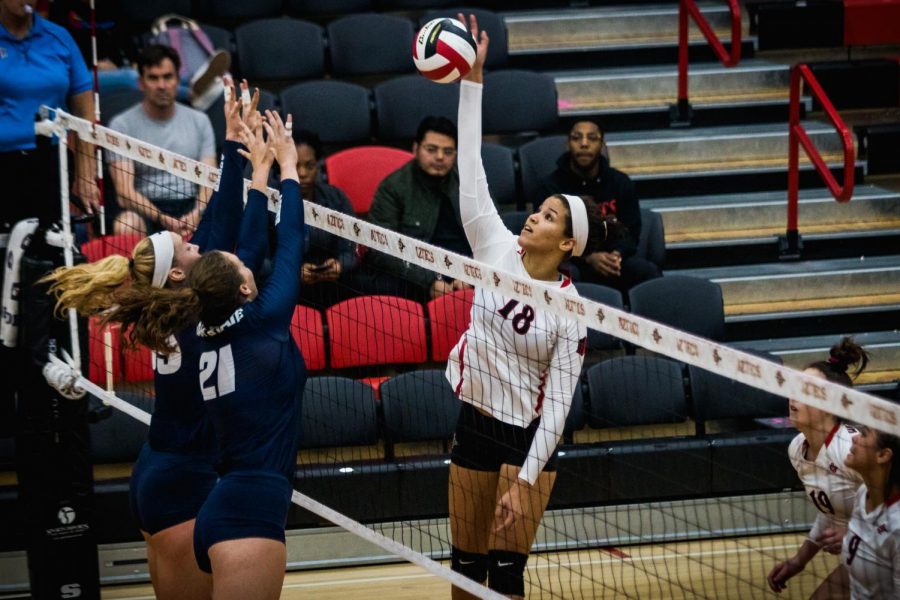 Junior middle blocker Tamia Reeves attempts to put the ball over the outstretched arms of two Utah State blockers during the Aztecs three-set victory over the Aggies on Nov. 1 at Peterson Gym. 