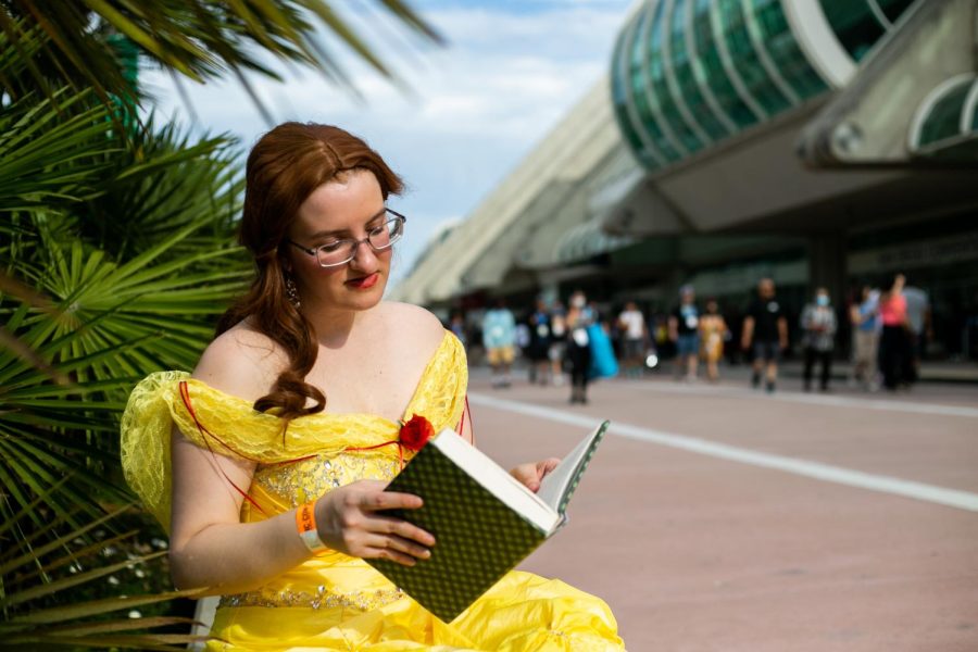 Samantha Fuller-Hall dressed as Belle from Beauty and the Beast pretends to read a book that is hollowed out amongst the bustling Comic-Con crowd.