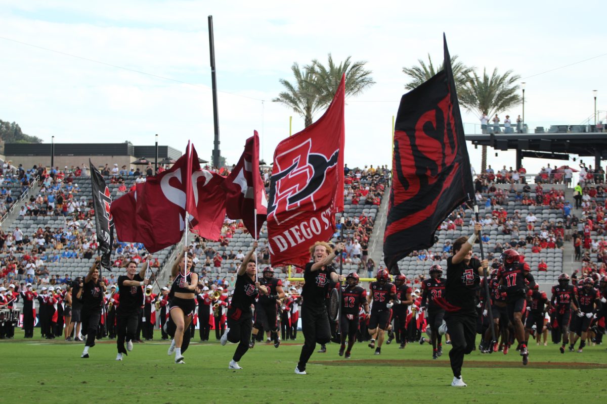 Members of the San Diego State cheerleading team lead the Aztecs football team onto the field before a game during the 2023 season at Snapdragon Stadium.