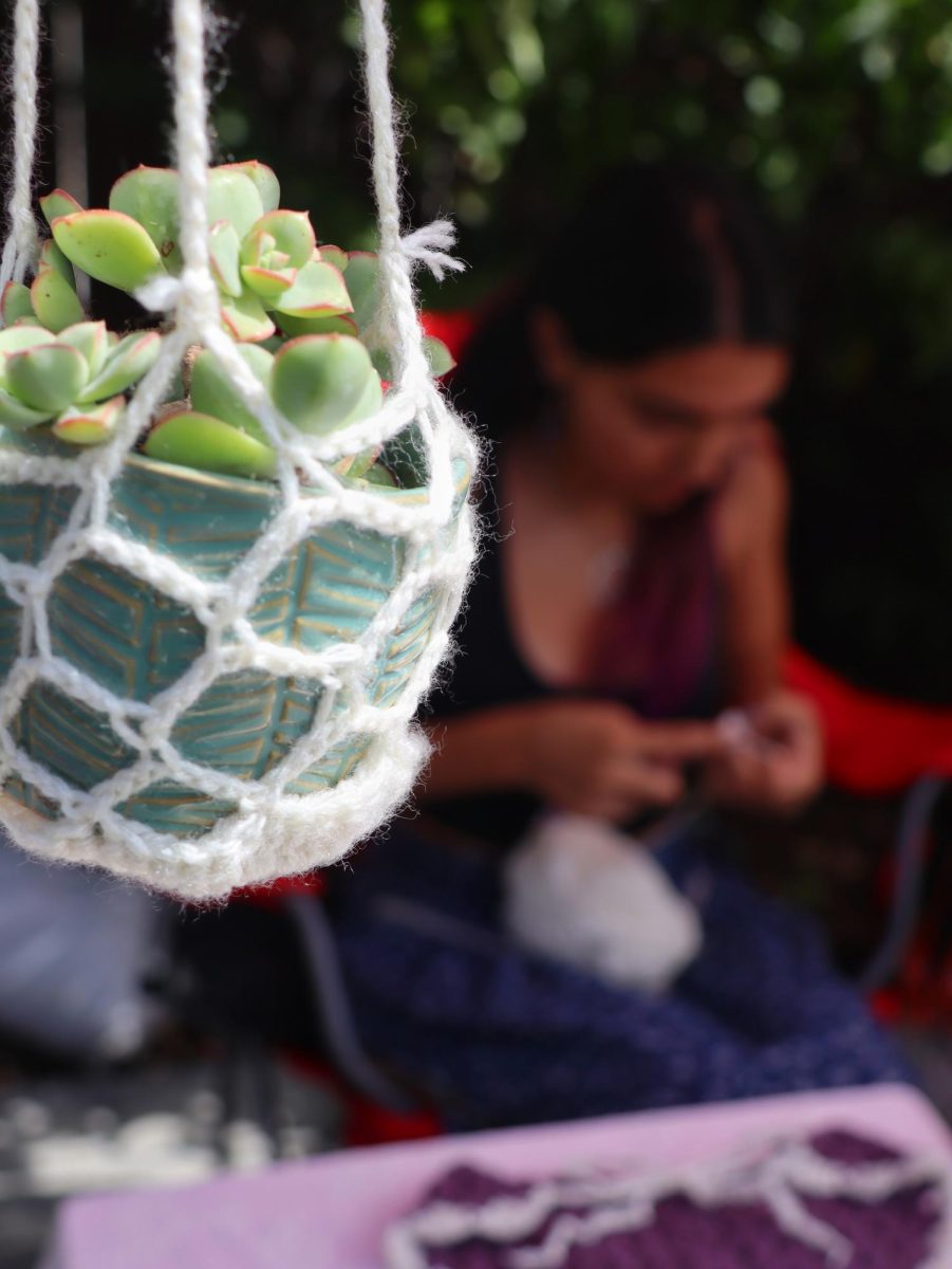 A vendor crochets their product while waiting for customers.