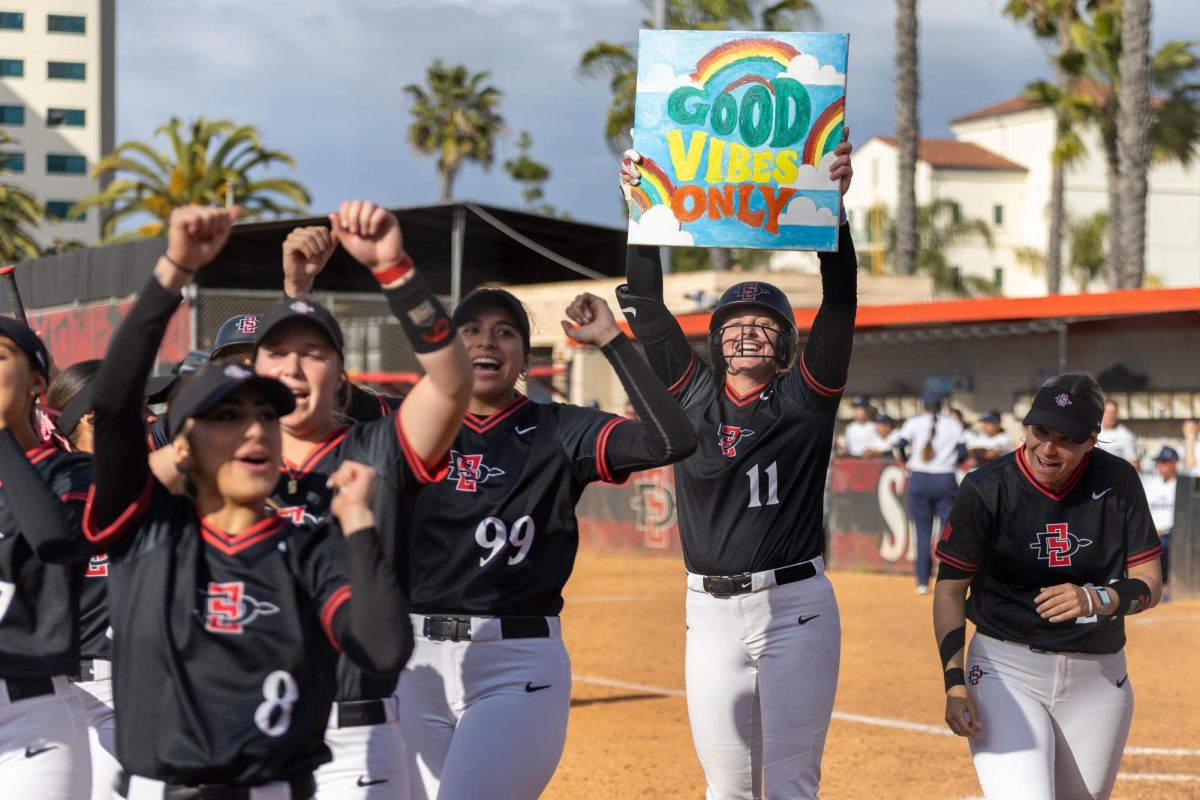 The San Diego State softball team runs off the field celebrating holding a Good Vibes Only sign earlier this season at SDSU Softball Stadium. The Aztecs cruised to a 14-1 mercy rule win over San Jose State on Friday, April 12. 