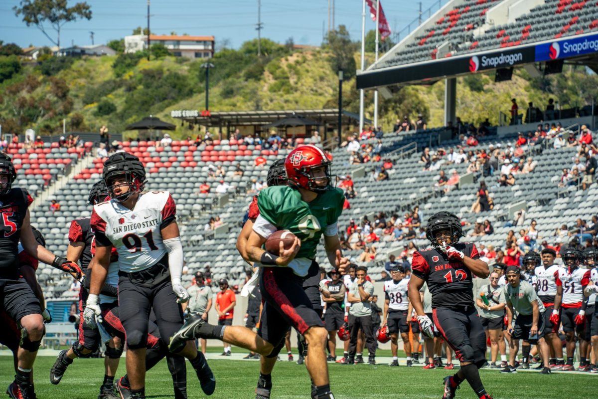 Quarterback Kyle Crum runs from cornerback Tayten Beyer and defensive lineman Keion Mitchell at SnapDragon Stadium on Saturday, April 20. The Aztecs played a scrimmage game, as part of the Aztec Fast Showcase. 
