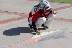 An attendee draws a symbol with the color of the Palestine flag — black, white, green and red, in front of Hepner Hall at SDSU on Tuesday, Oct. 8, 2024, .