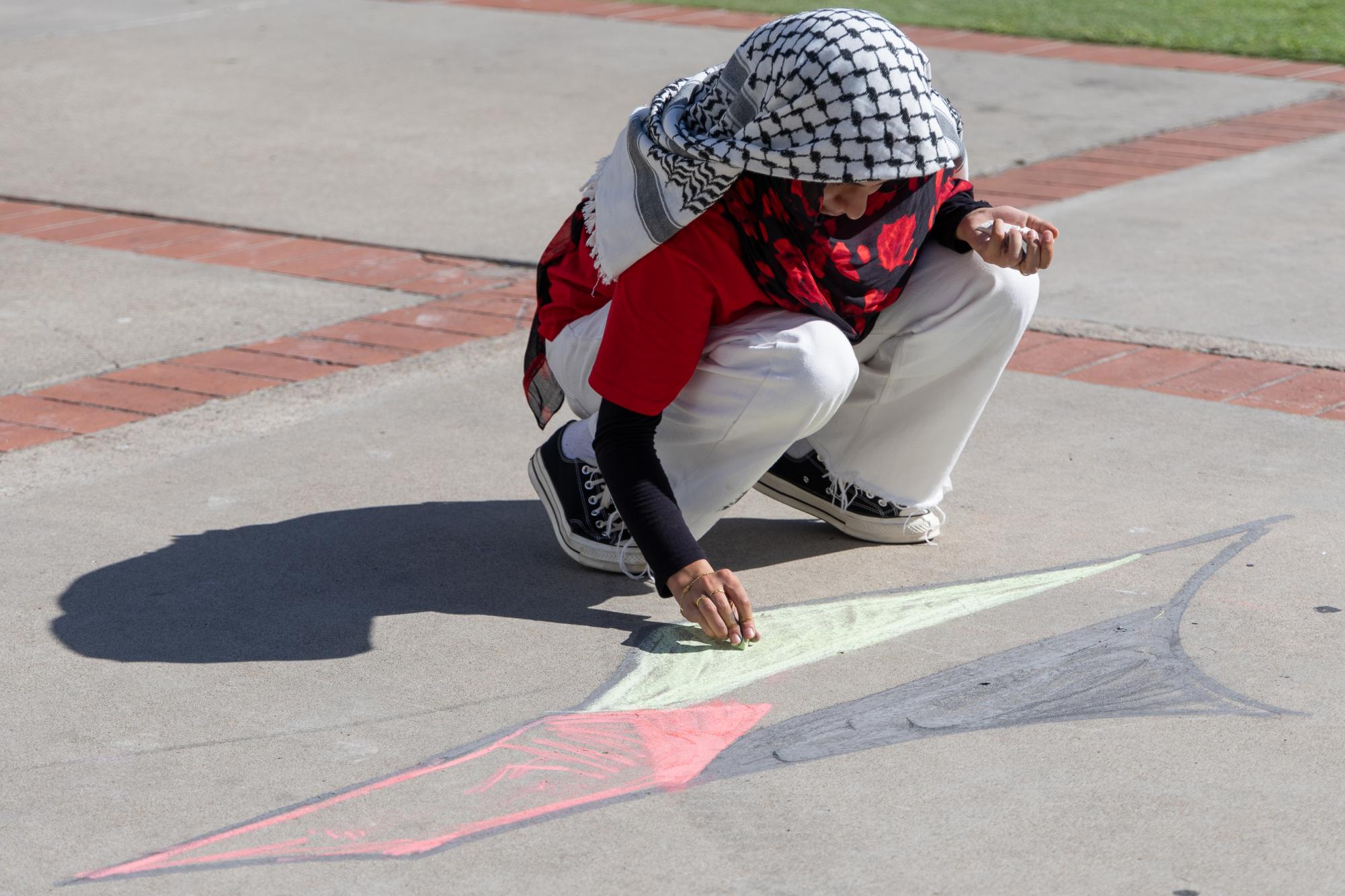 An attendee draws a symbol with the color of the Palestine flag — black, white, green and red, in front of Hepner Hall at SDSU on Tuesday, Oct. 8, 2024, .
