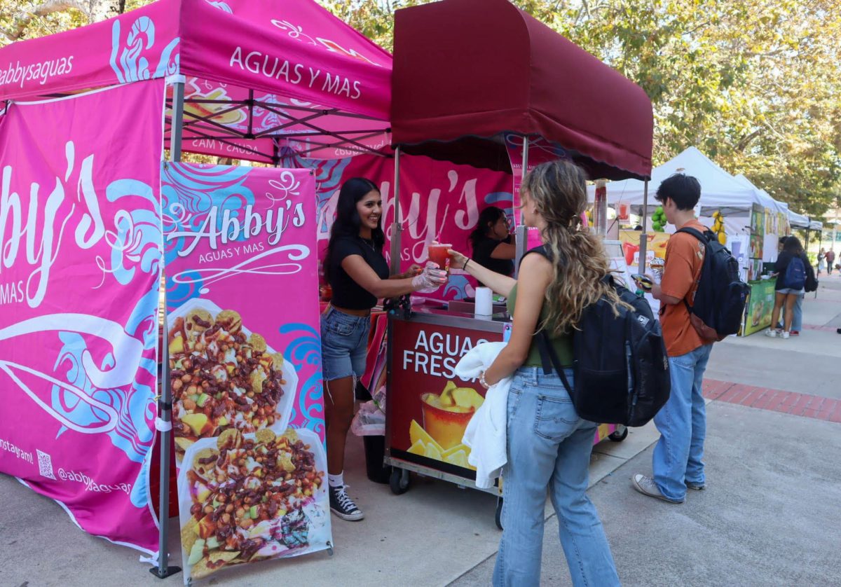 Abigail Carrera, dueña de Abby's Aguas Y Mas, le entrega alegremente su bebida a un cliente en el Mercadillo de SDSU el 3 de octubre de 2024. 