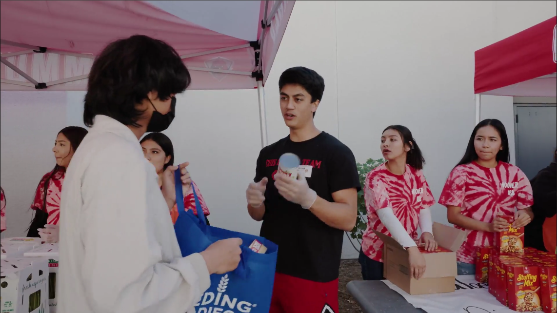 San Diego State guard Kimo Ferrari helps pass food out to children and families in need at Hoover High School. Image Courtesy of the MESA Foundation. 